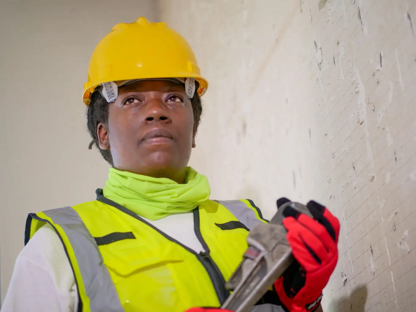 Construction worker in a yellow hard hat and hi-vis vest holding a wrench