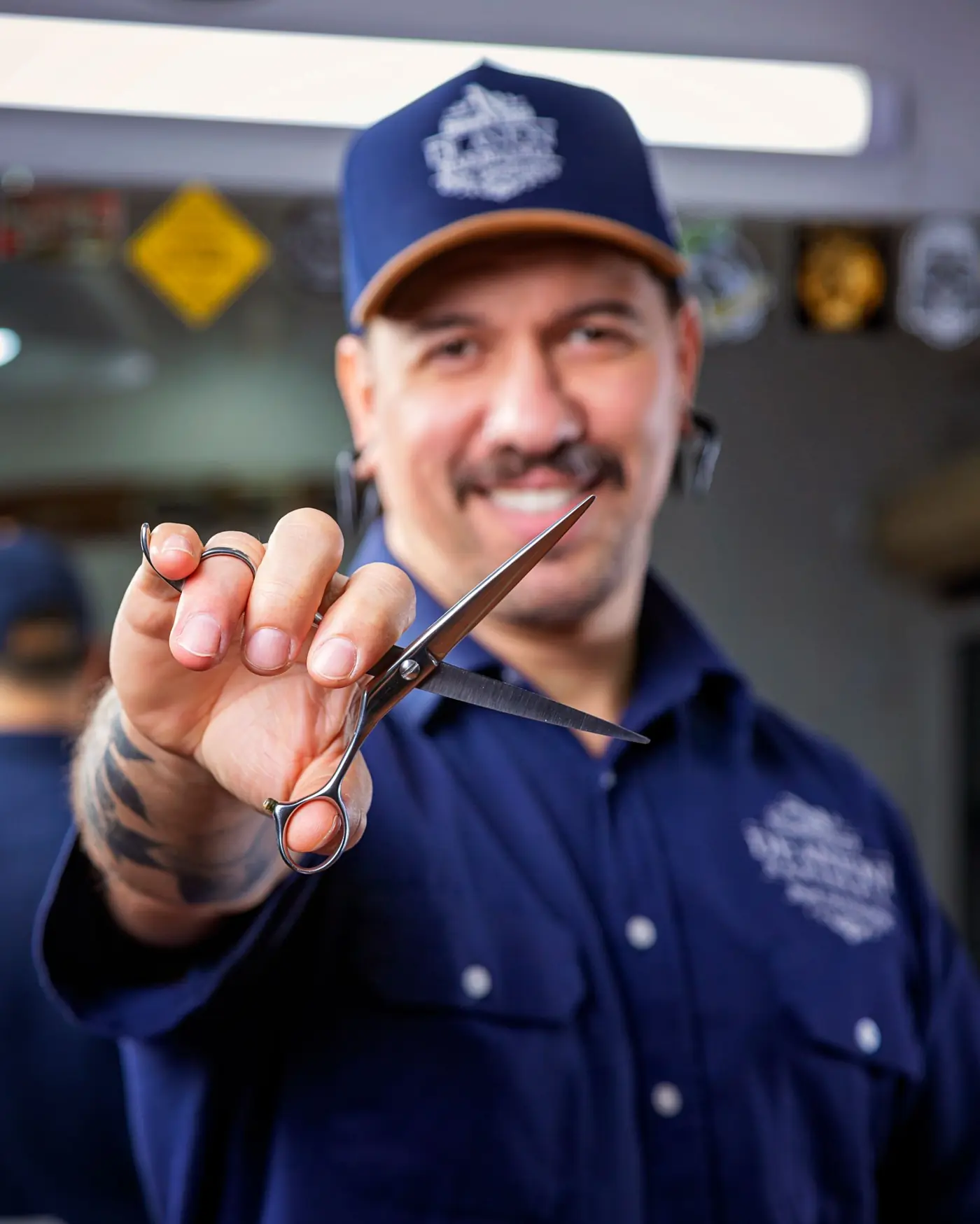 Smiling barber holding scissors in his own barbershop